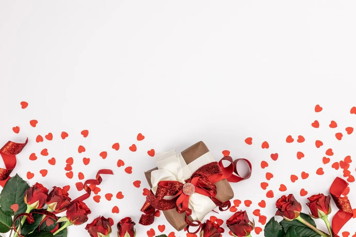 Flatlay auf weißem Hintergrund mit Geschenkbox und Details der Valentinstagsdekoration.